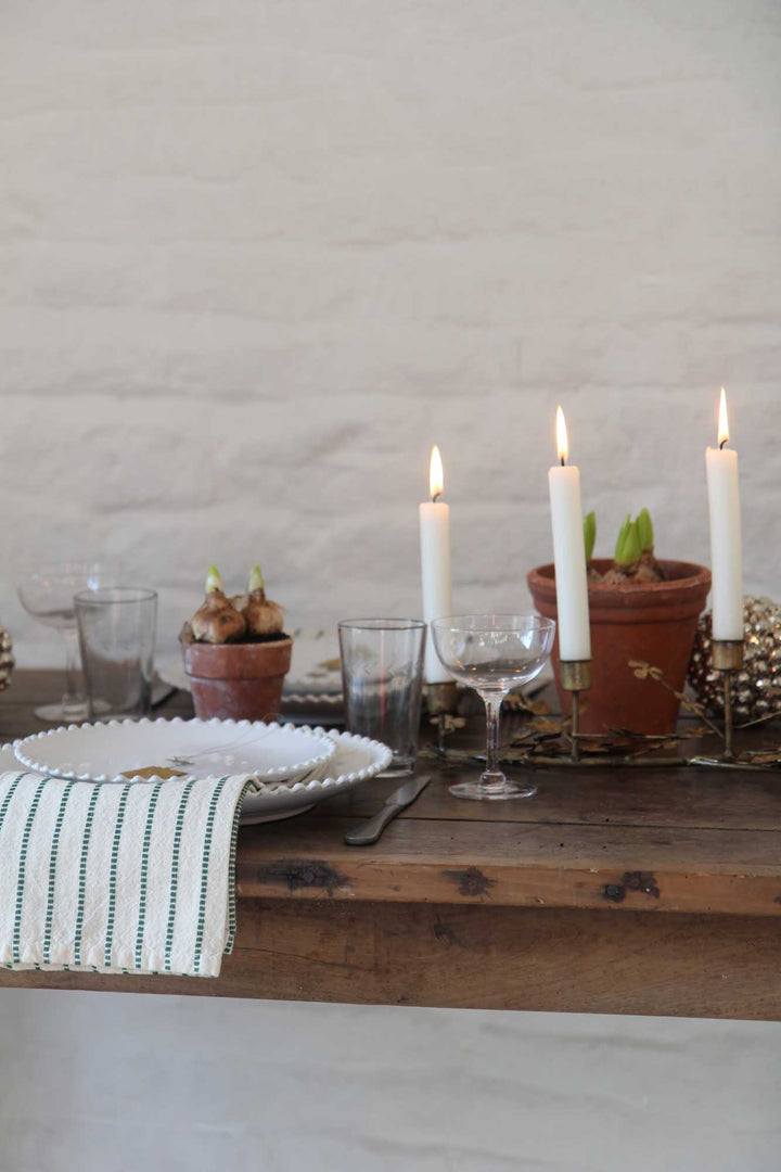 Dining table setup with candles, plates, and glasses on a wooden surface.