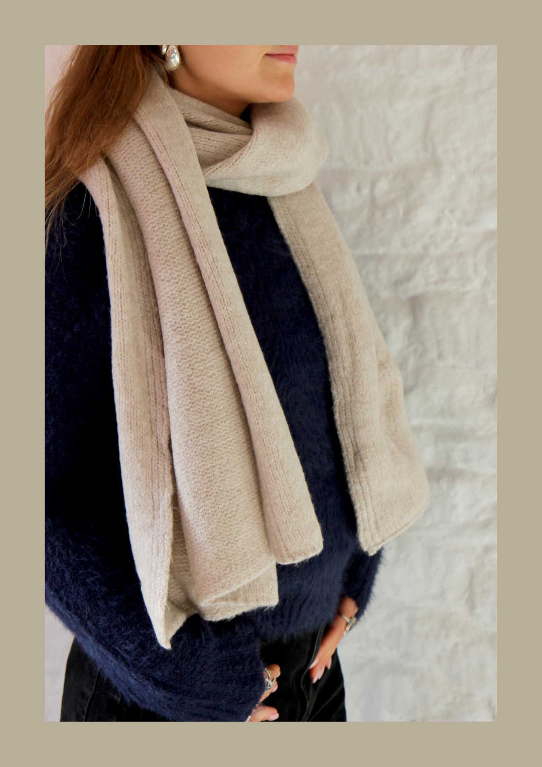 Person wearing a beige scarf and navy sweater against a neutral background