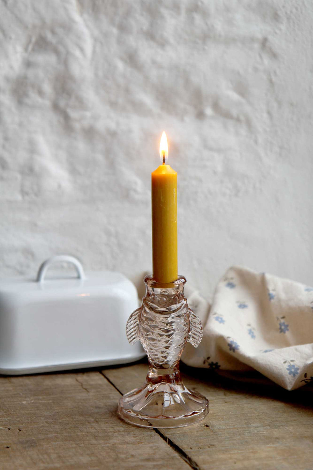 Candle in a glass holder on a wooden surface with a white textured wall background
