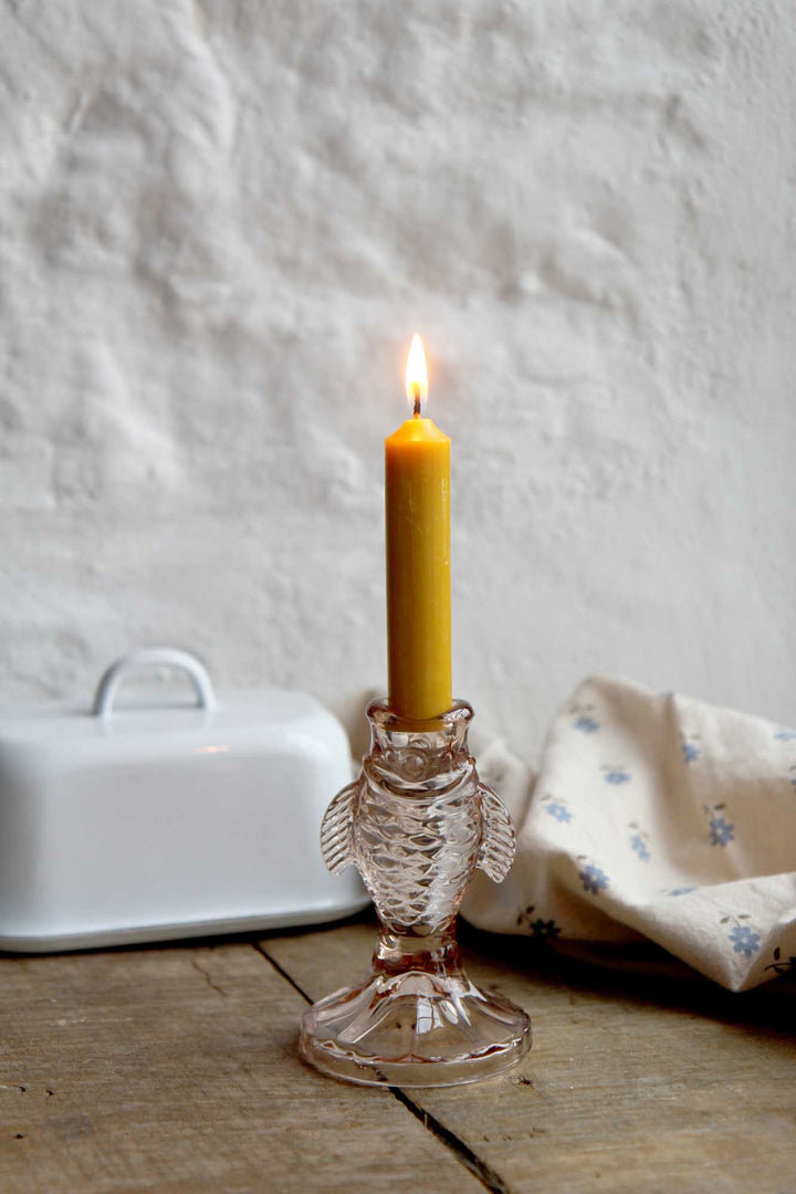 Candle in a glass holder on a wooden surface with a white textured wall background