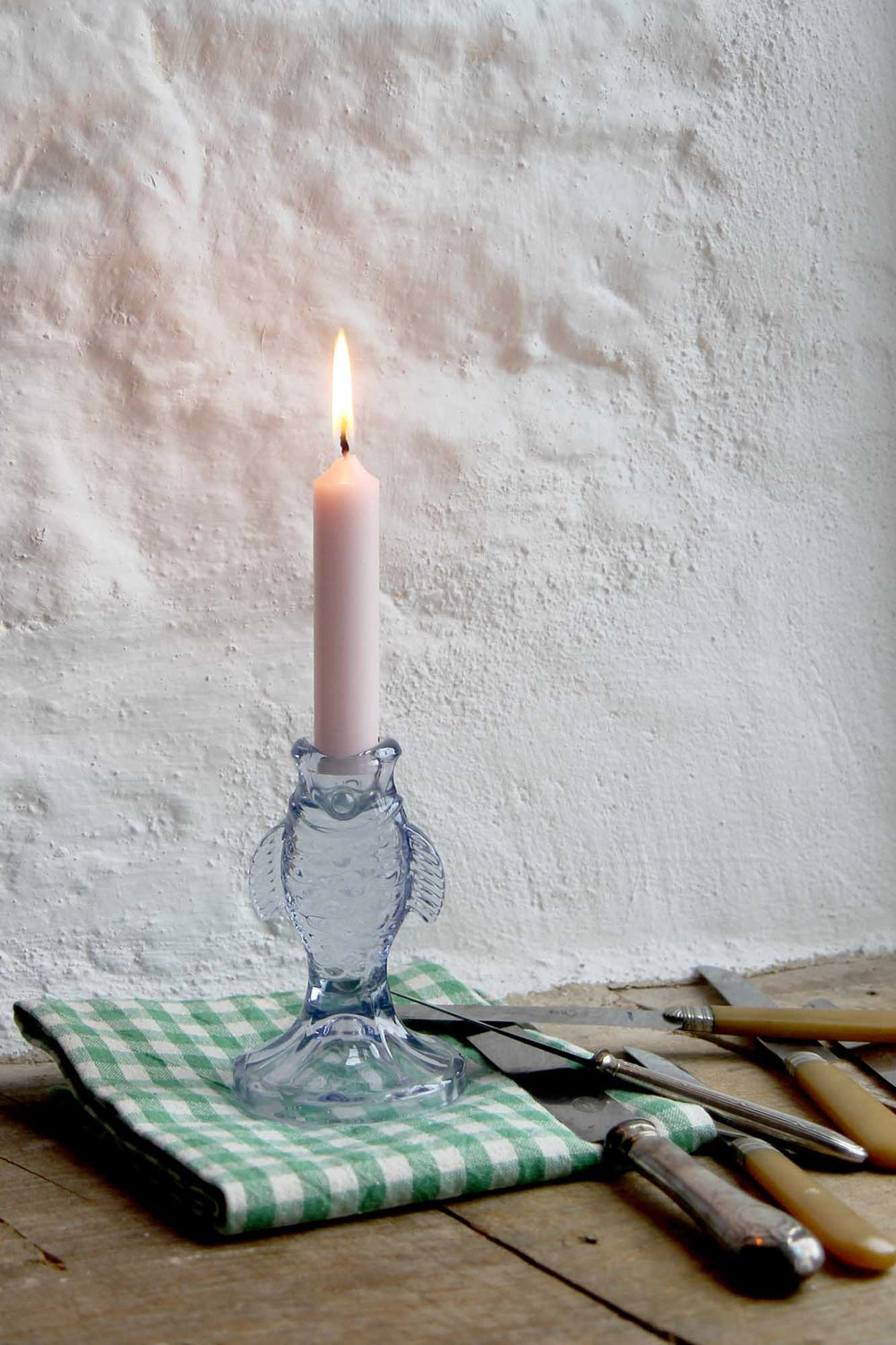 Glass fish-shaped candle holder with a lit candle on a wooden surface with tools.