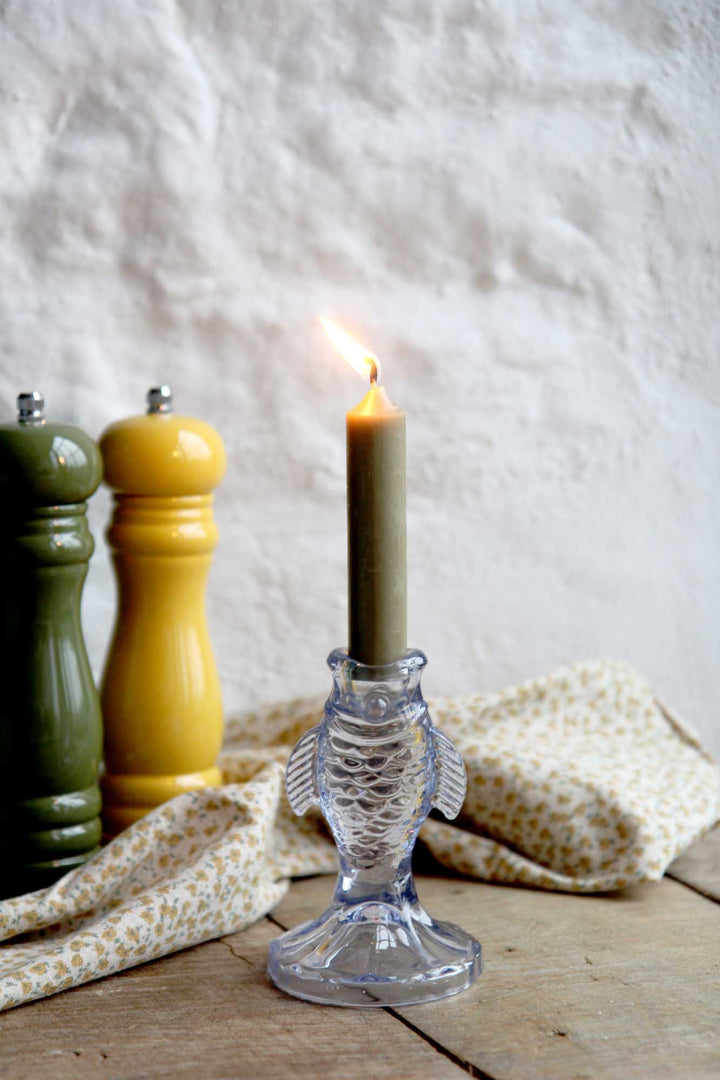 Glass fish-shaped candle holder with a lit candle on a wooden surface with salt and pepper shakers.
