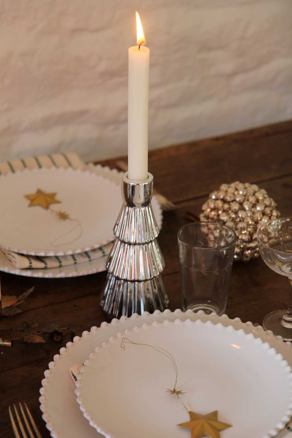 Candle in a decorative holder on a table with plates and glasses.