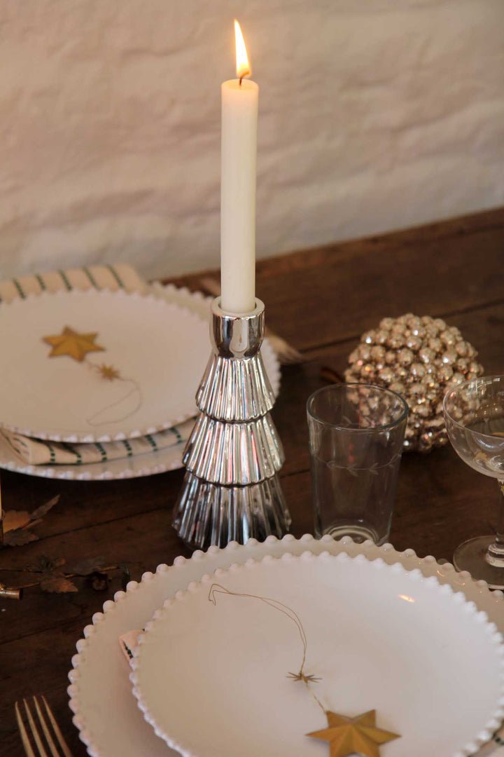 Candle in a decorative holder on a table with plates and glasses.