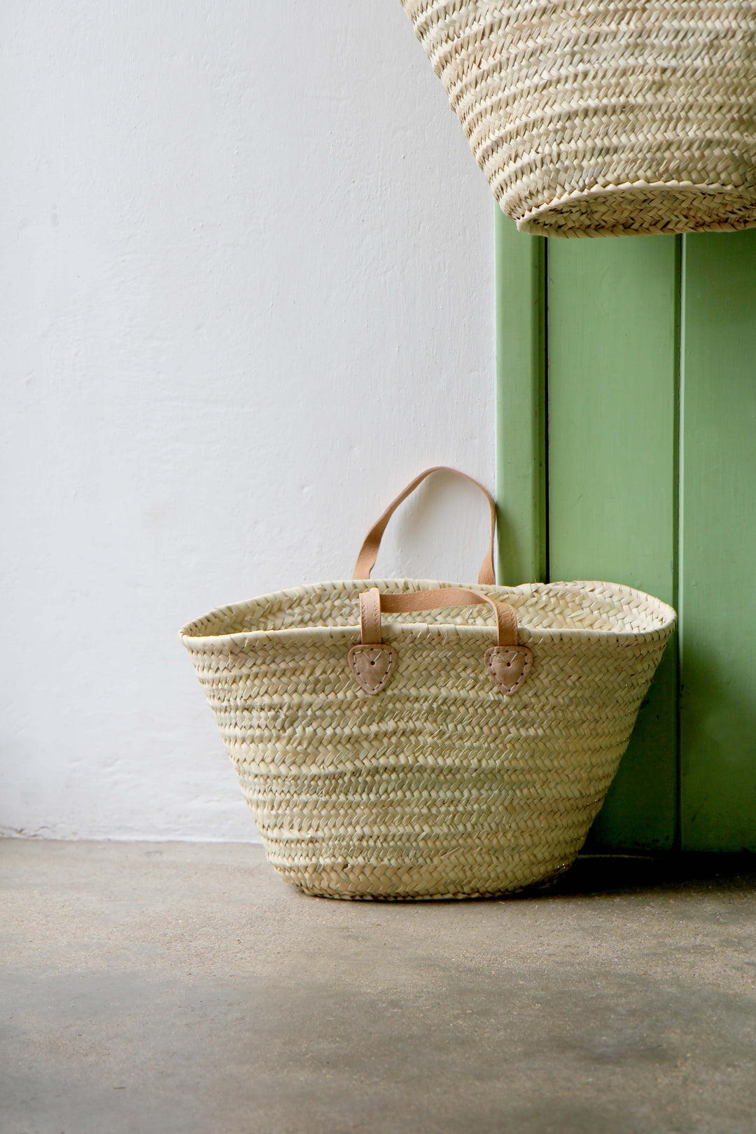 Woven basket with leather handles against a green wall.
