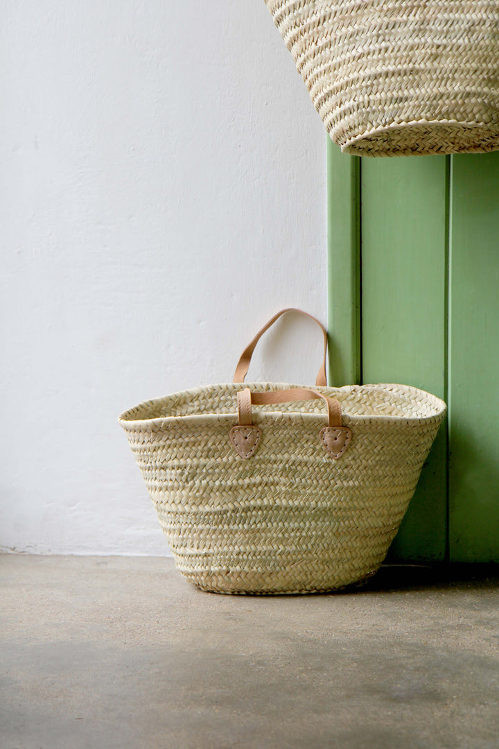 Woven basket with leather handles against a green wall.