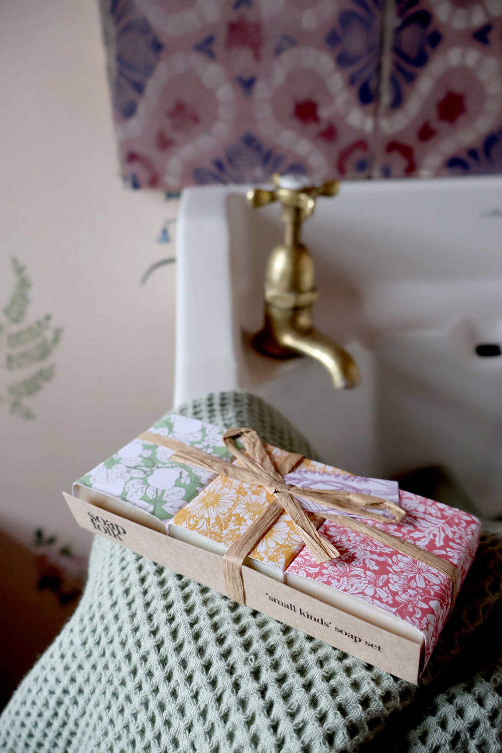Set of soap bars in decorative packaging on a textured surface with a patterned lamp in the background.