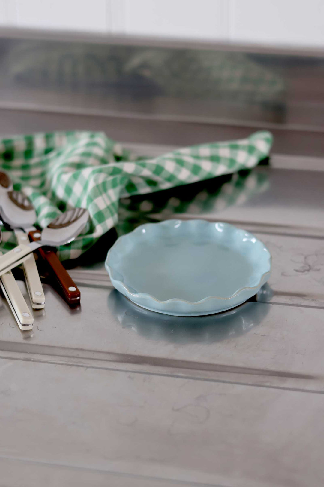 Light blue ceramic plate on a wooden surface with a green checkered cloth and utensils in the background.
