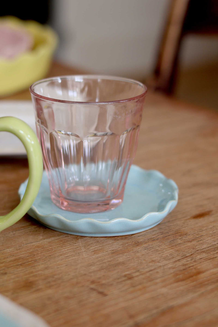 Clear glass on a light blue saucer with a green handle on a wooden surface