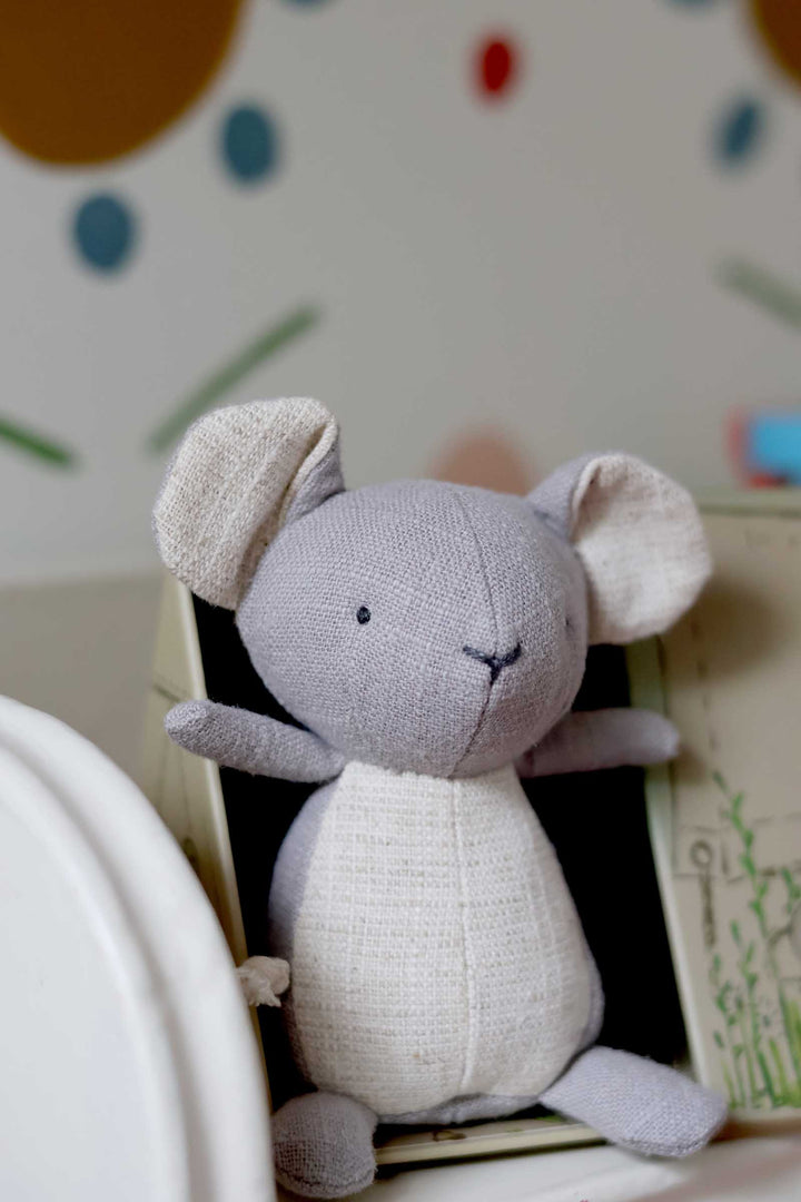 Gray plush mouse toy with white accents on a polka dot background