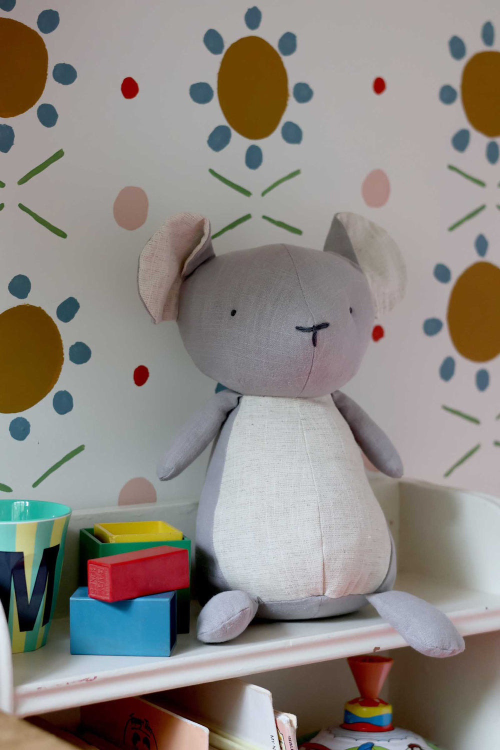 Stuffed animal toy on a shelf with colorful blocks against a floral-patterned wall.