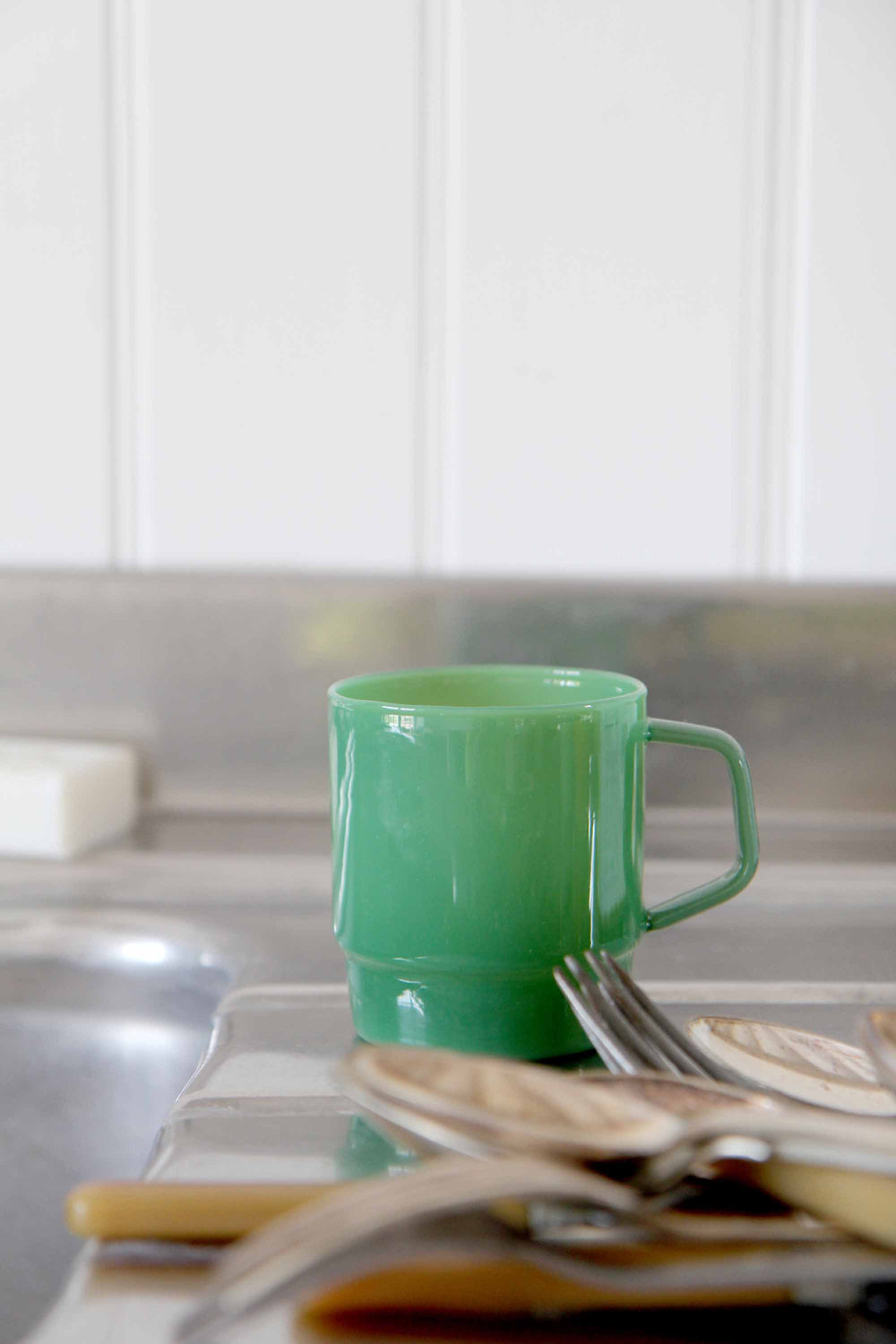 Green mug on a kitchen counter with utensils and a blurred background