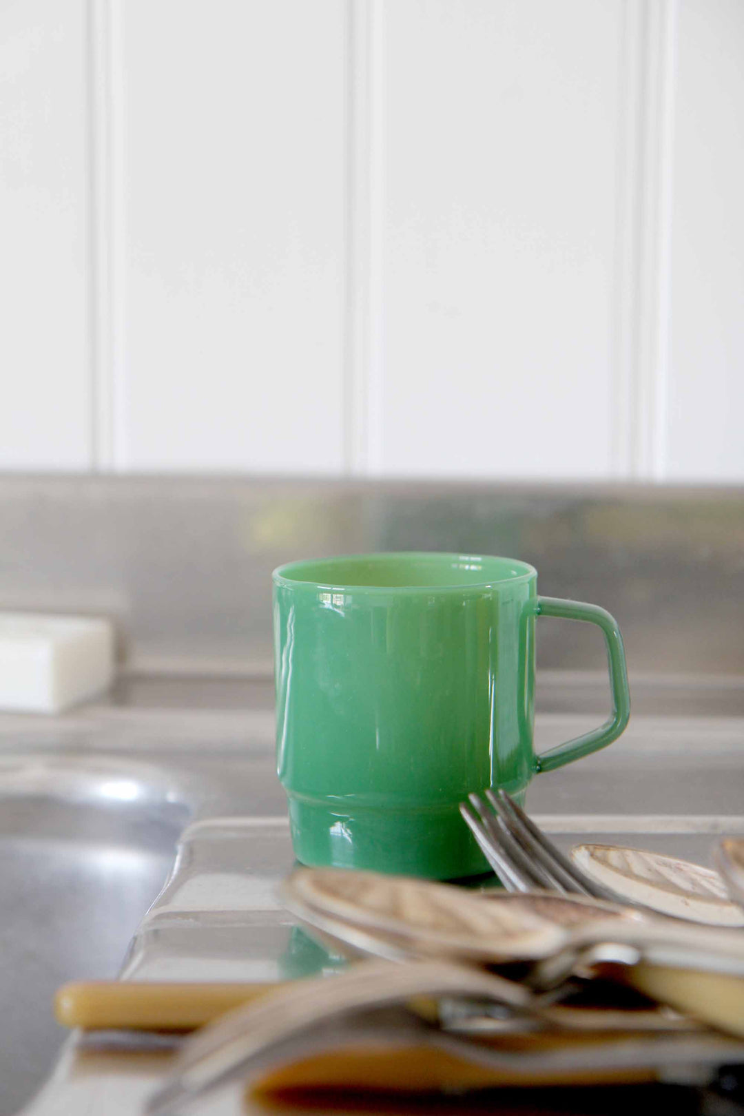 Green mug on a kitchen counter with utensils and a blurred background