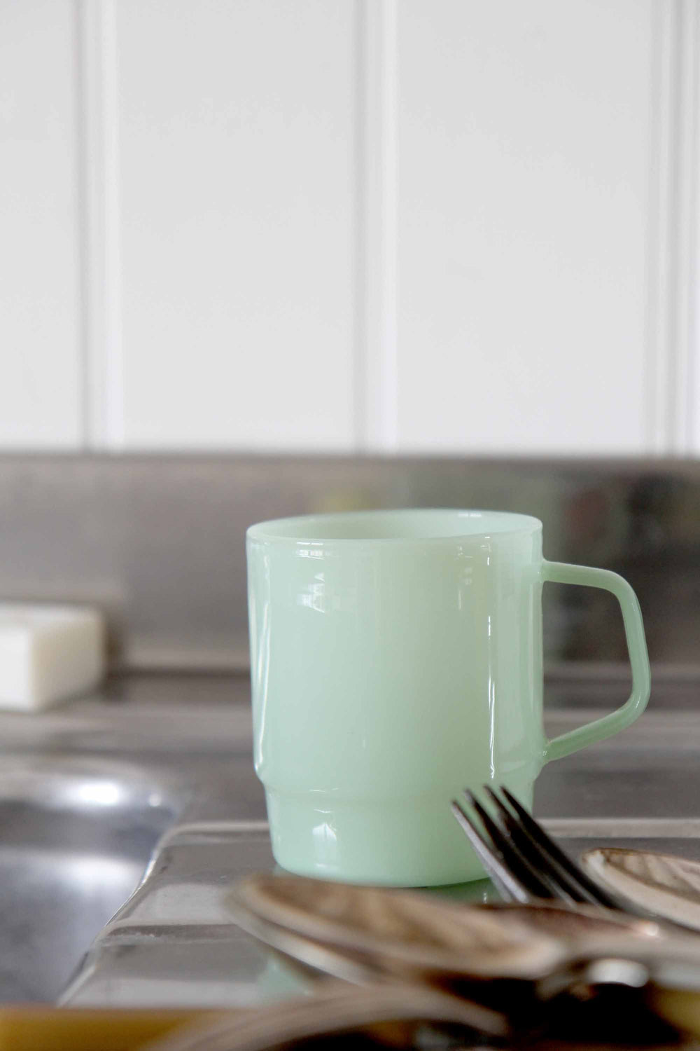 Green mug on a kitchen counter with utensils and a blurred background
