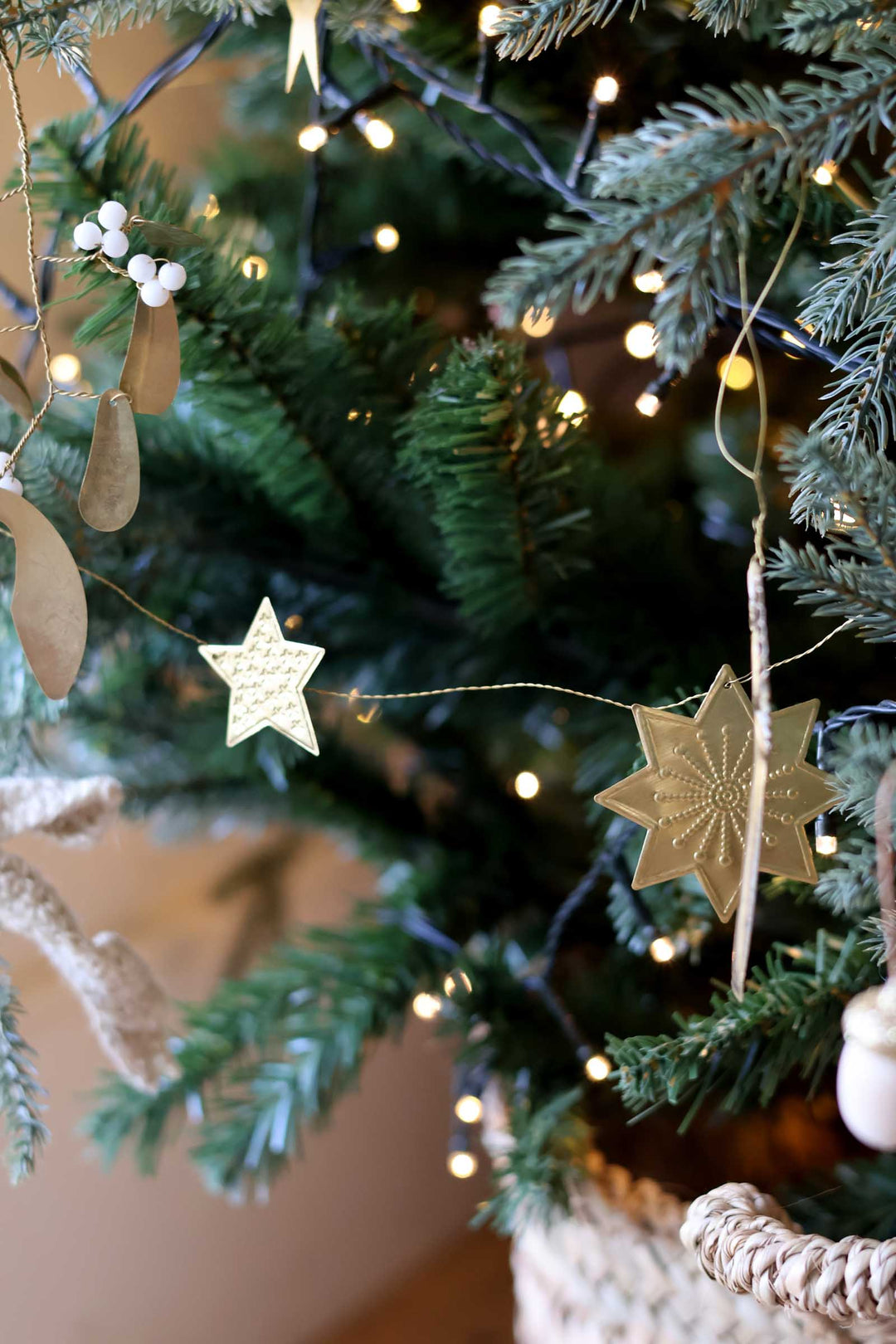 Close-up of a decorated Christmas tree with green pine branches, warm white string lights, and hanging gold-toned star ornaments.