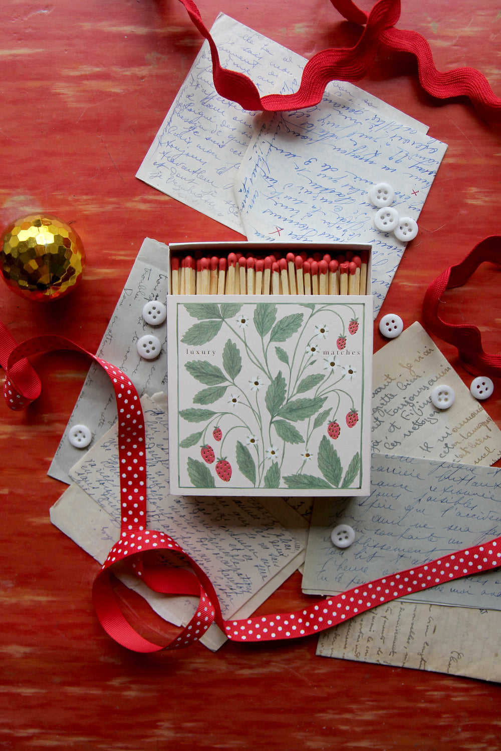 Decorative matchbox with floral design on a red surface with ribbons and cards.