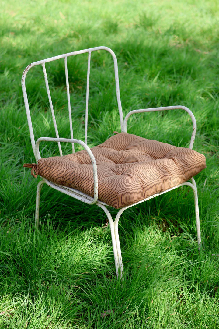White metal chair with a brown cushion on a grassy background