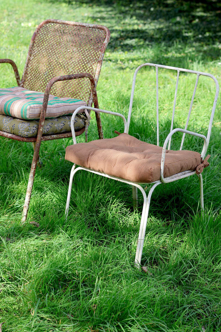 Two metal chairs with cushions on a grassy outdoor setting