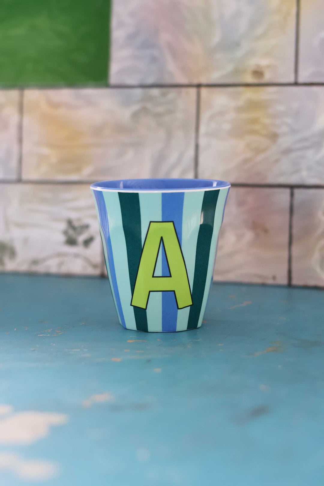 Striped cup with letter 'A' on a blue surface and tiled wall background