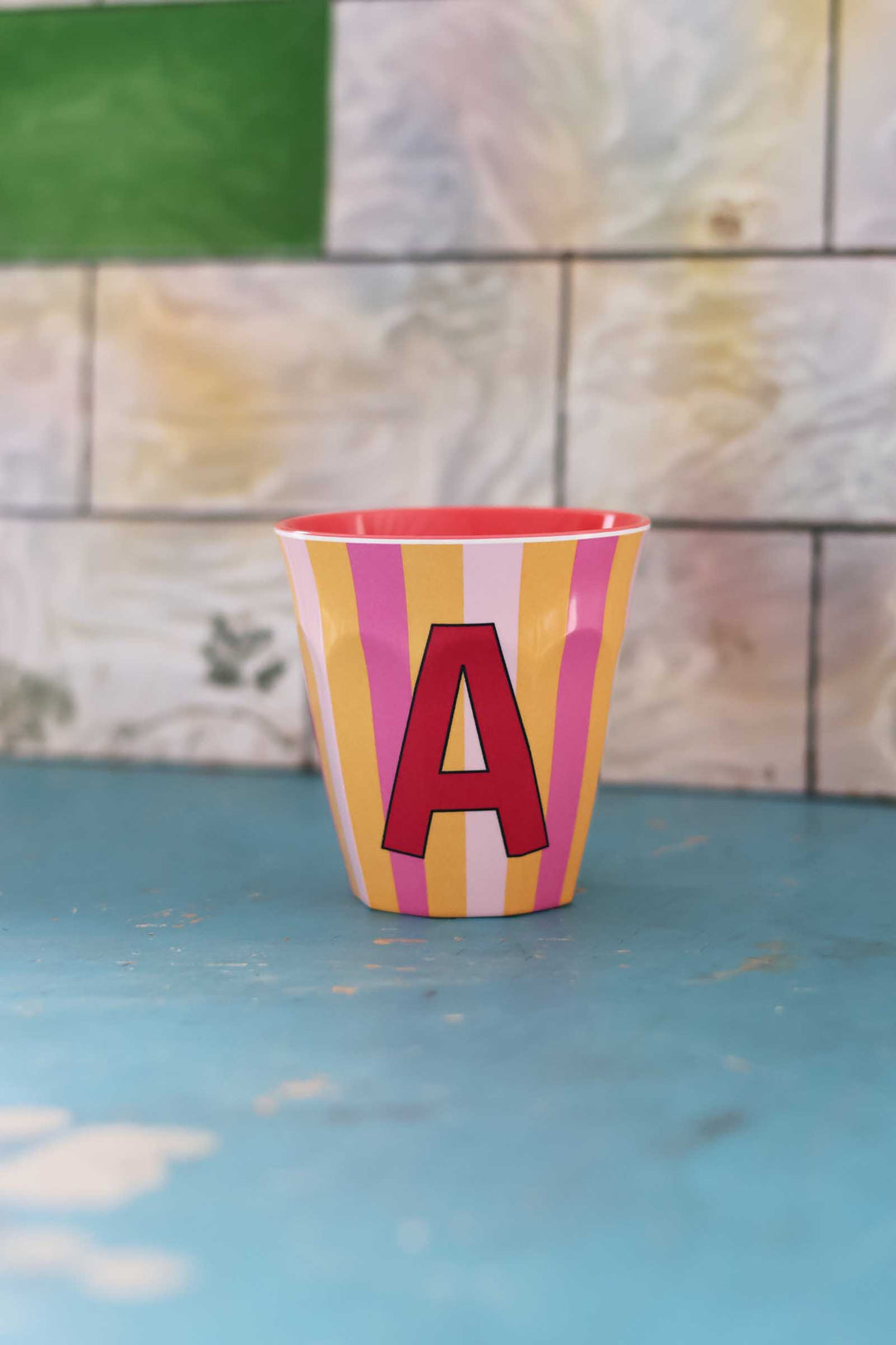 Striped cup with letter 'A' on a tiled wall background