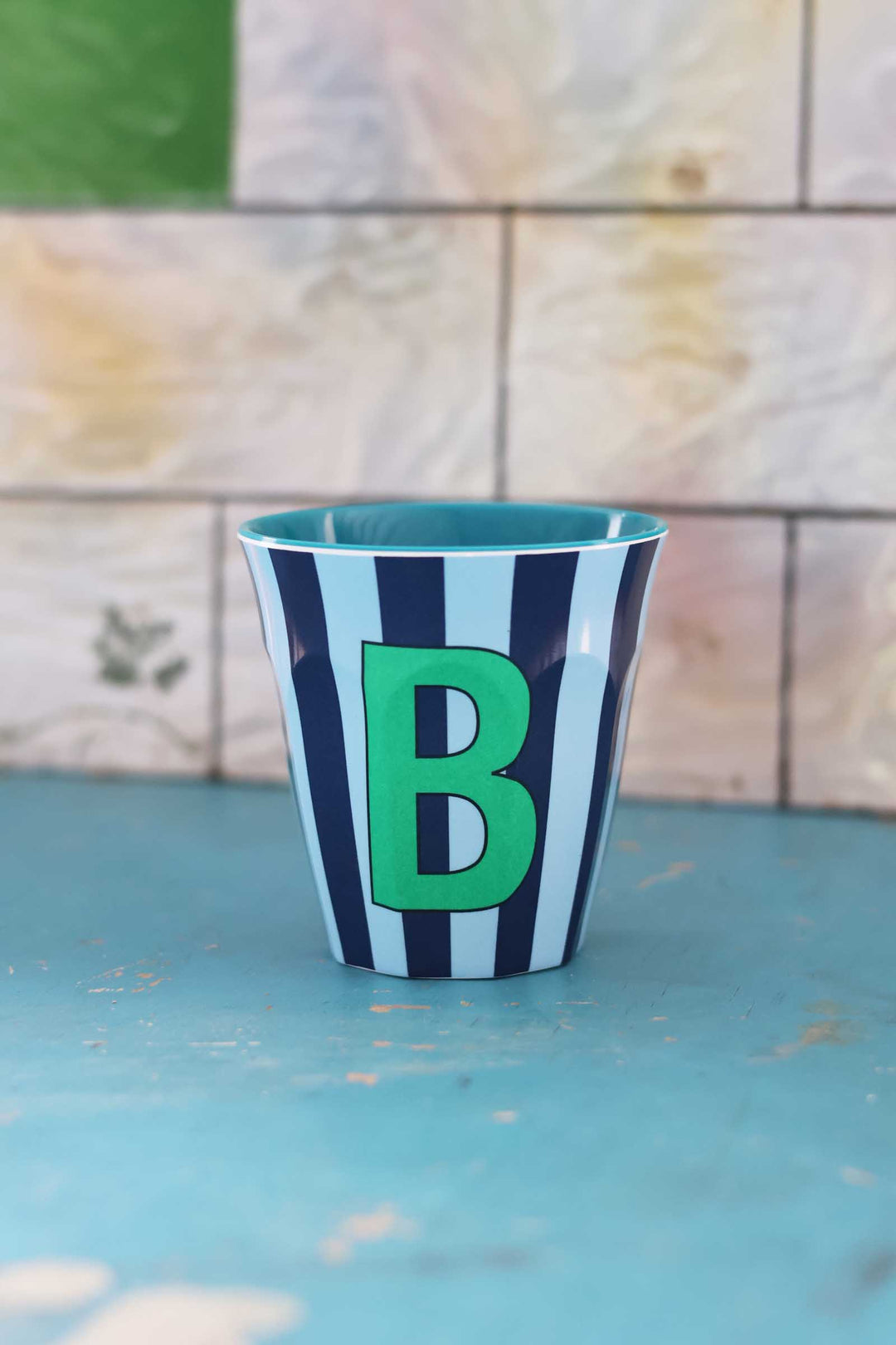 Striped cup with a green letter 'B' on a blue surface