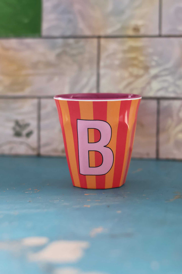 Striped cup with letter 'B' on a blue surface and tiled wall background