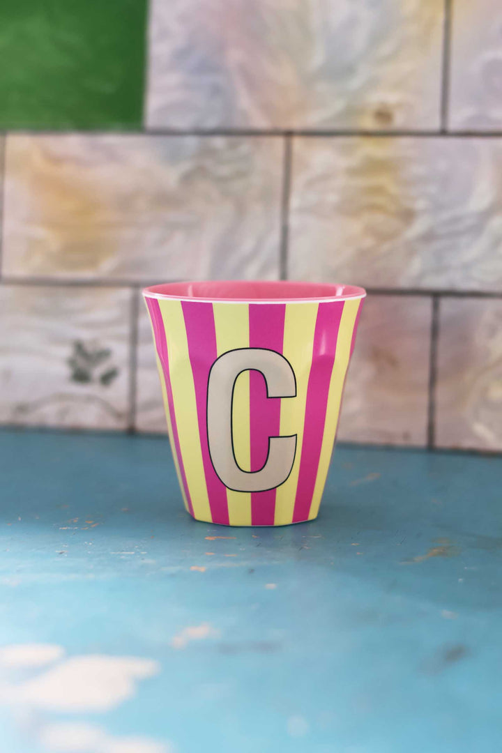 Striped cup with letter 'C' on a blue surface and tiled wall background