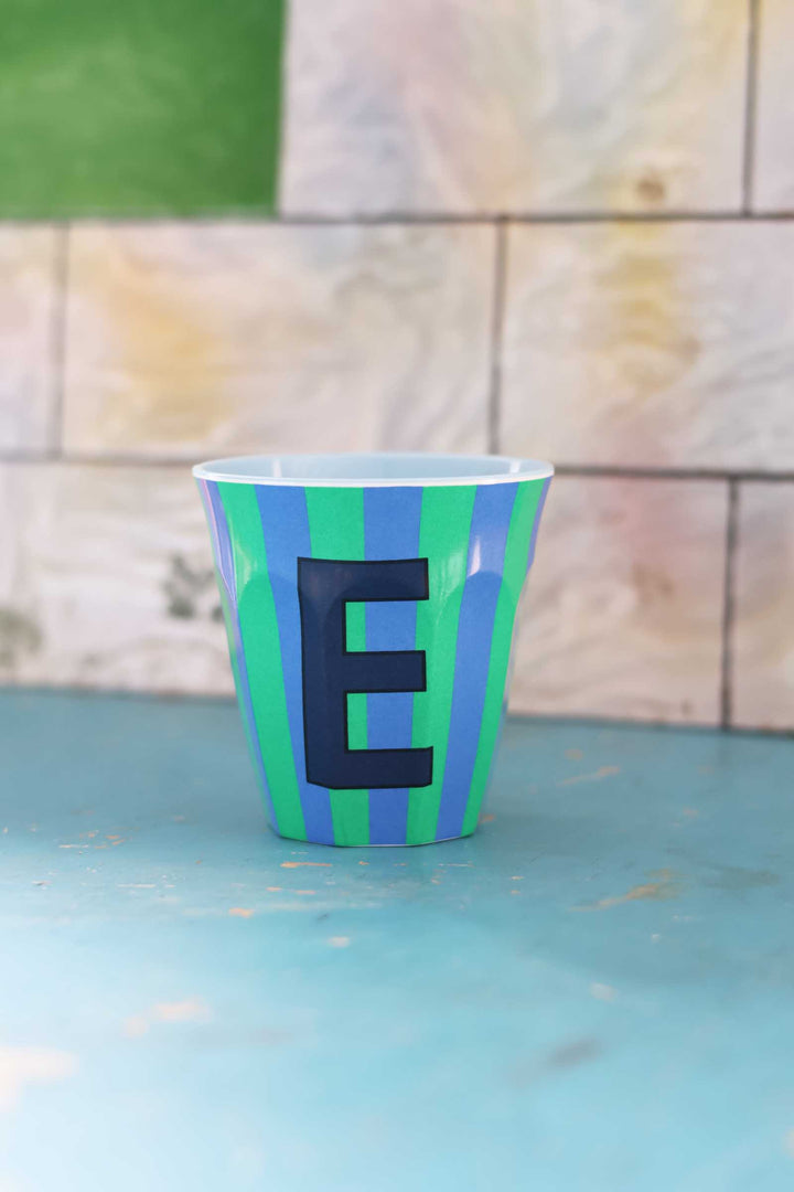 Green and blue striped cup with letter 'E' on a light blue surface
