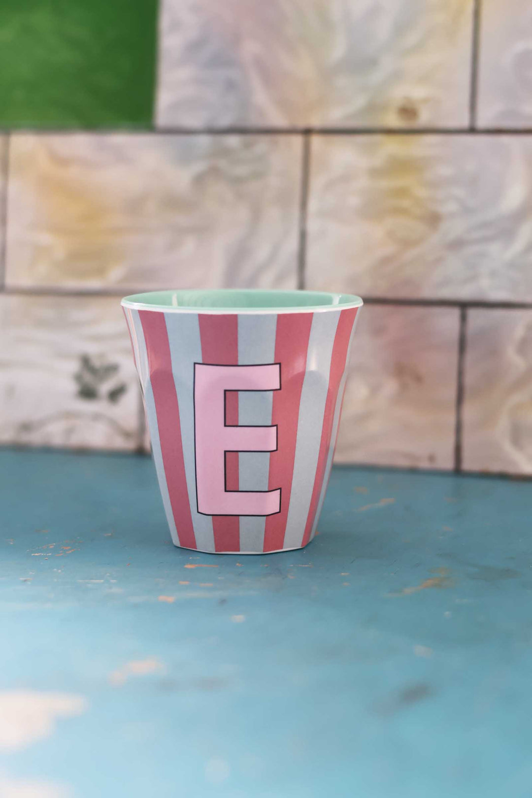 Striped mug with a pink letter 'E' on a blue surface and tiled wall background