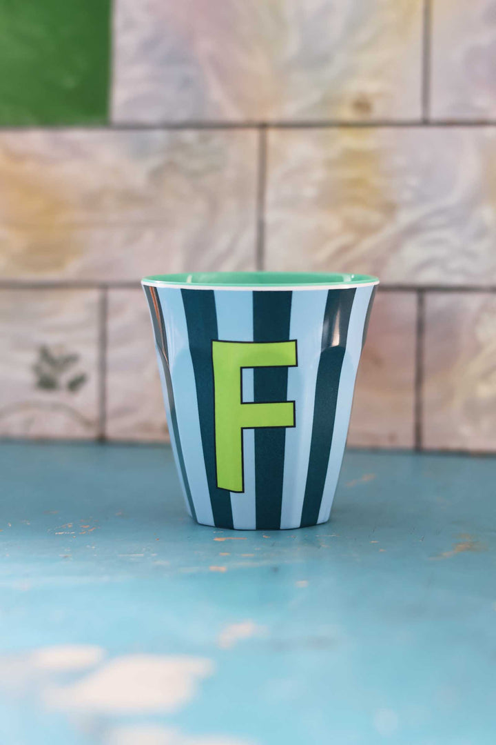 Striped cup with a green letter 'F' on a blue surface