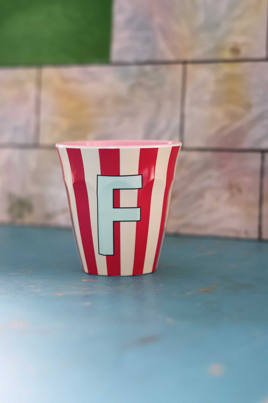 Striped cup with letter 'F' on a blue surface and patterned wall background