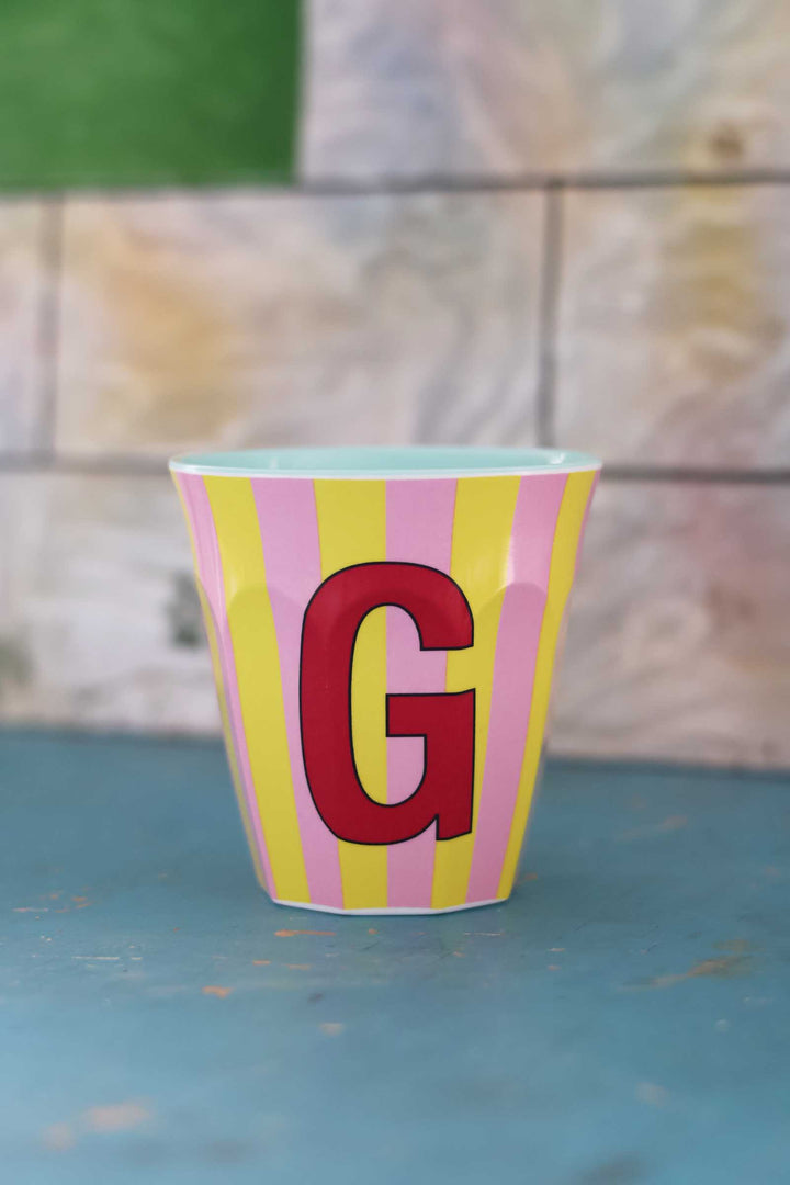 Striped cup with a red 'G' on a textured surface