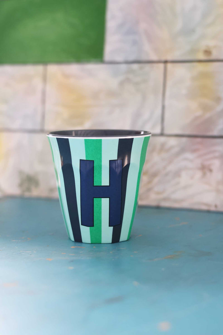 Striped cup with letter 'H' on a blue surface and tiled wall background