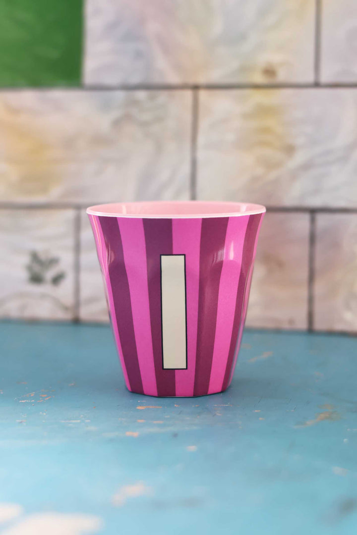 Pink and purple striped cup with a white label on a blue surface and tiled wall background