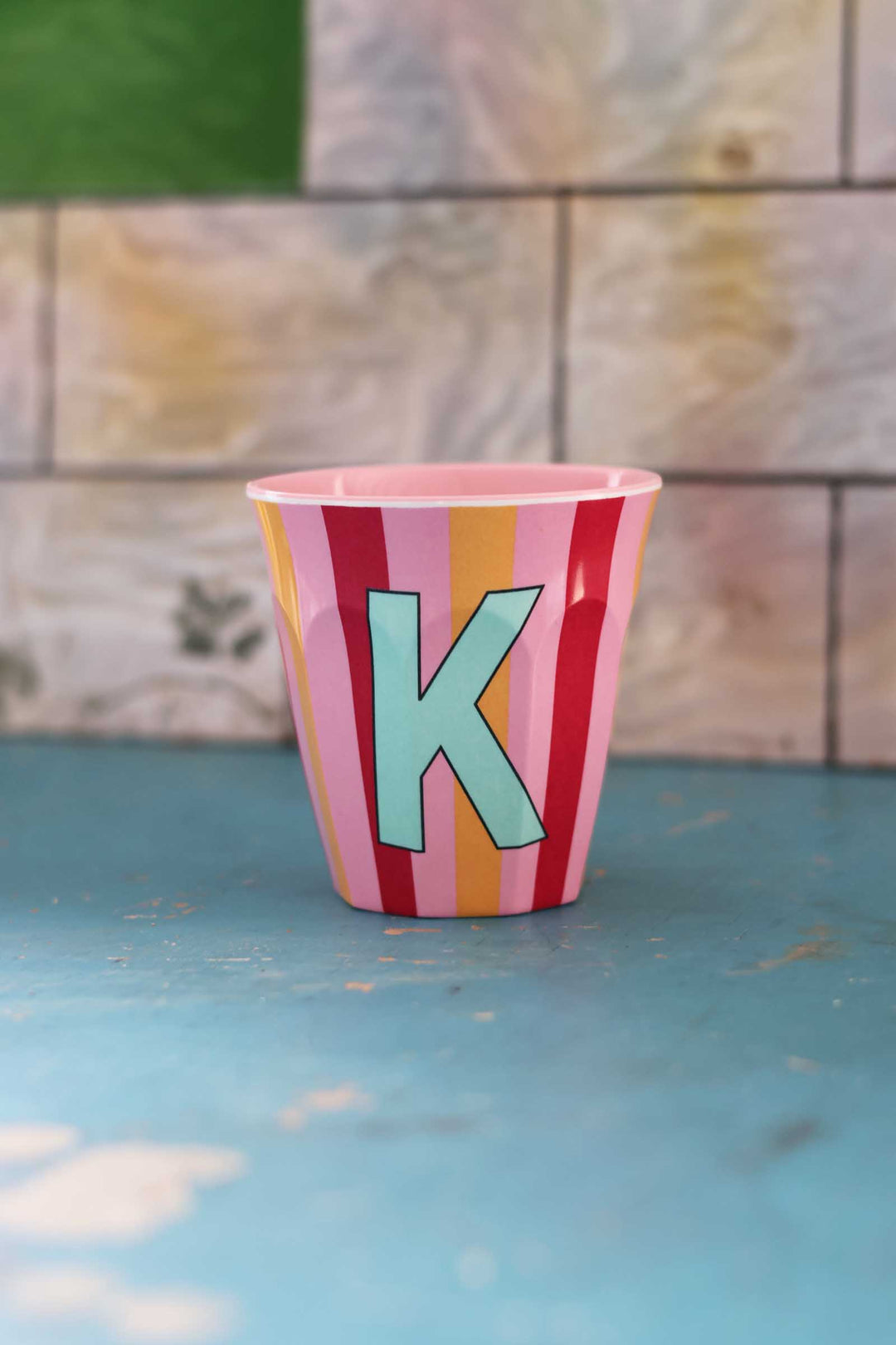 Colorful striped cup with a letter 'K' on a textured surface