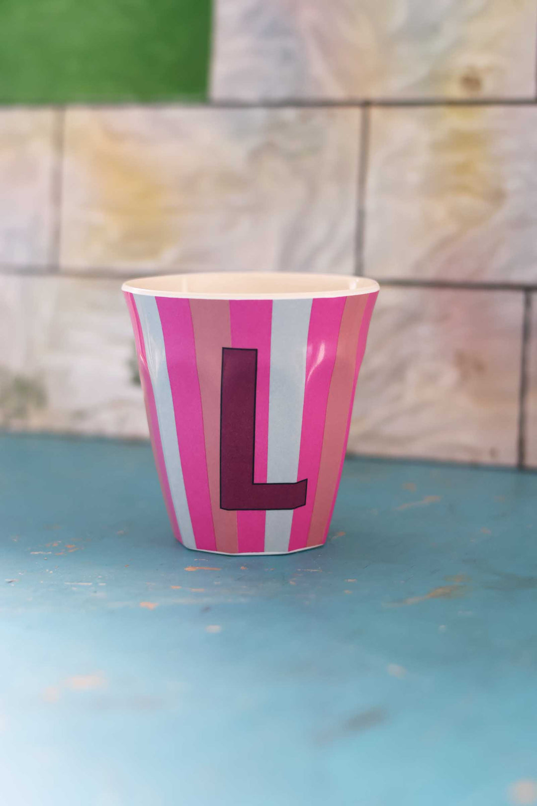 Striped cup with a letter 'L' on a blue surface and tiled wall background