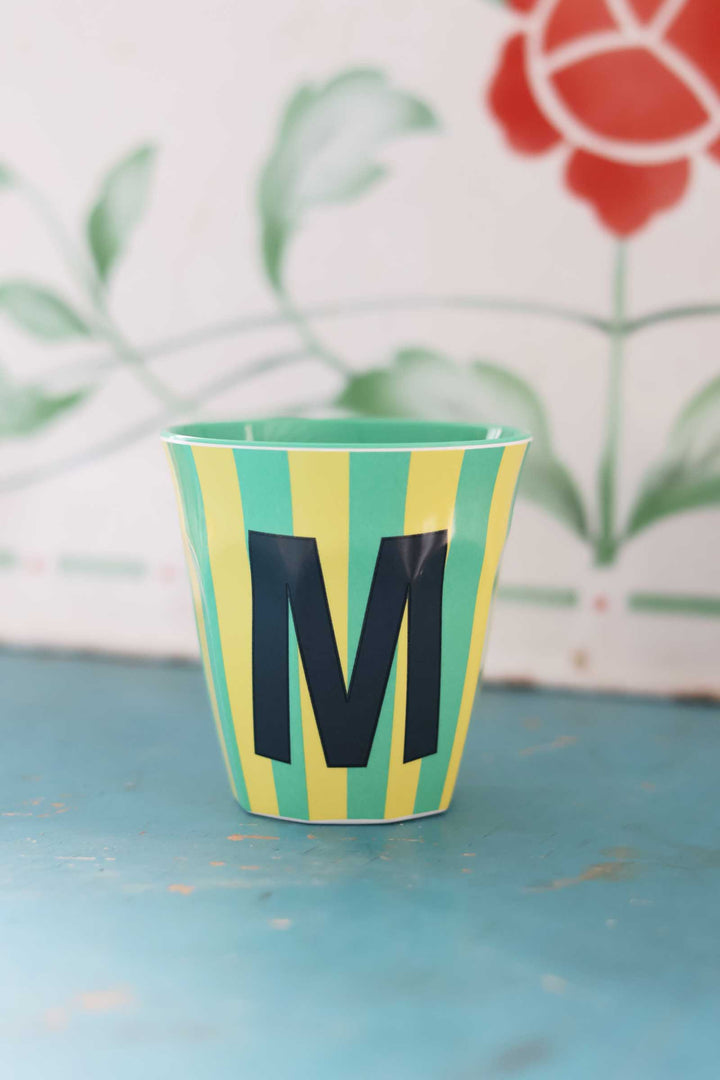 Colorful cup with letter 'M' on a blue surface, floral background