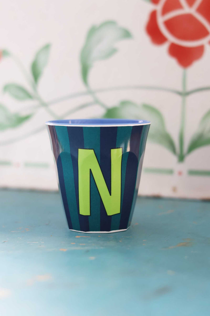 Blue cup with green letter 'N' on a blue surface with floral background