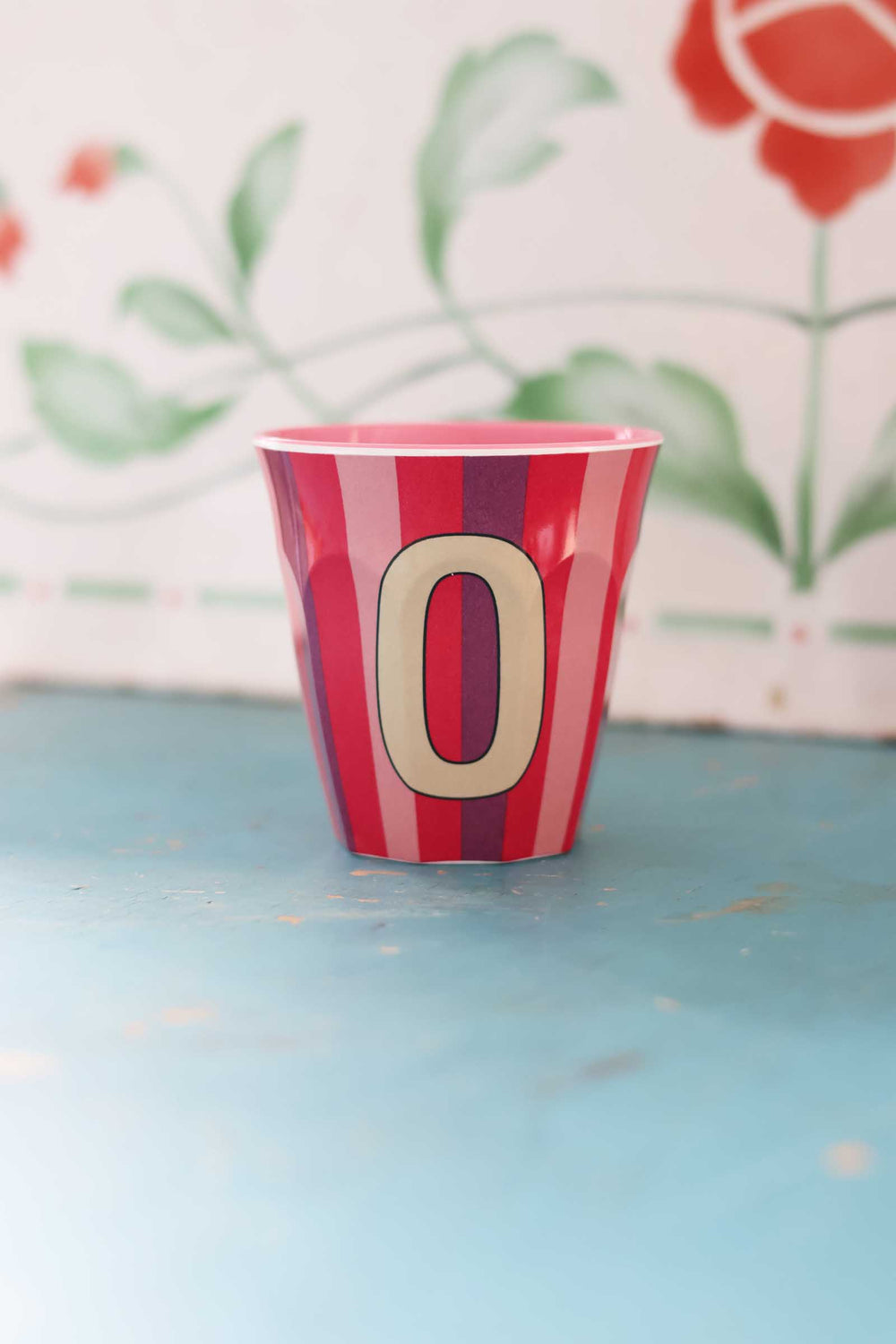 Red and white striped container with a beige number '0' on a blue surface with floral background