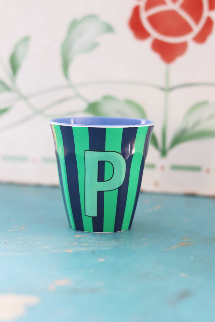 Green and blue striped cup with letter 'P' on a light blue surface