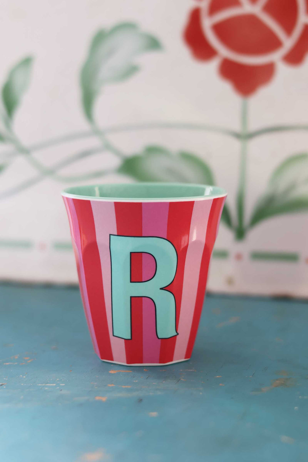 Striped cup with letter 'R' on a blue surface with floral background