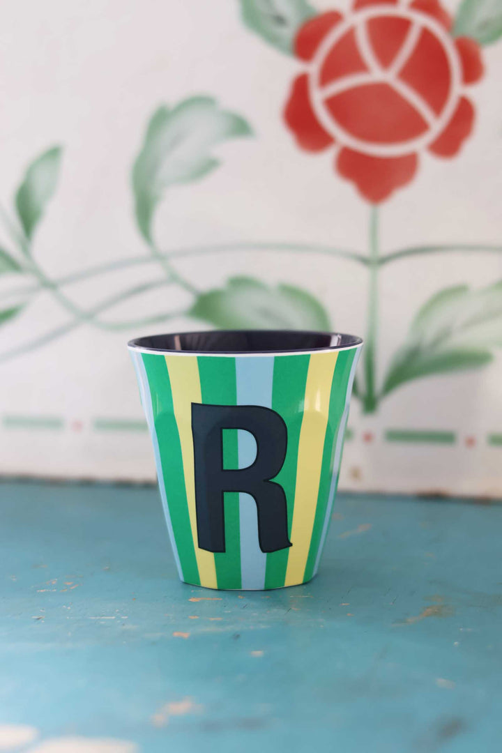 Colorful cup with letter 'R' on a blue surface and floral background