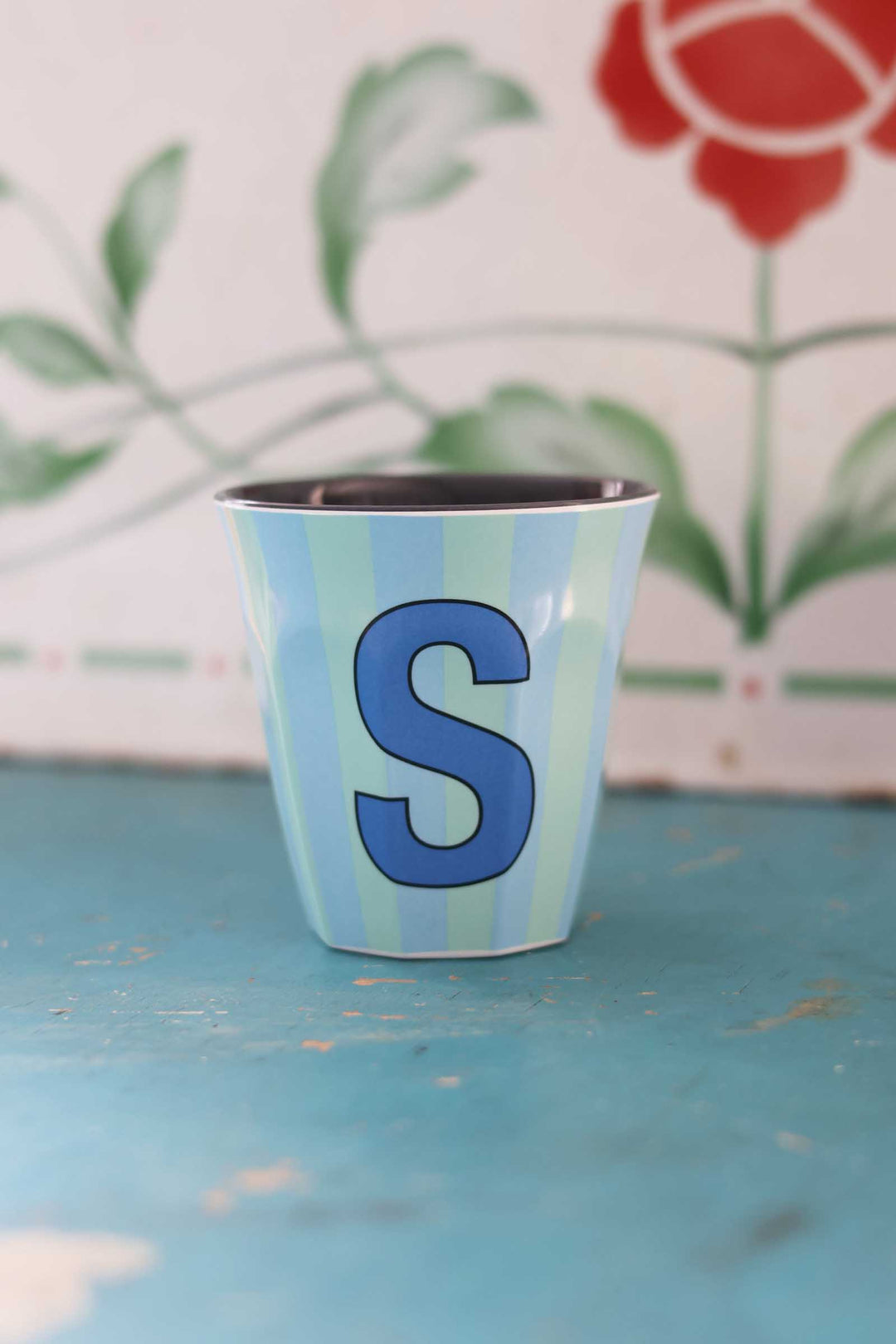 Small cup with a blue letter 'S' on a textured surface with a floral background