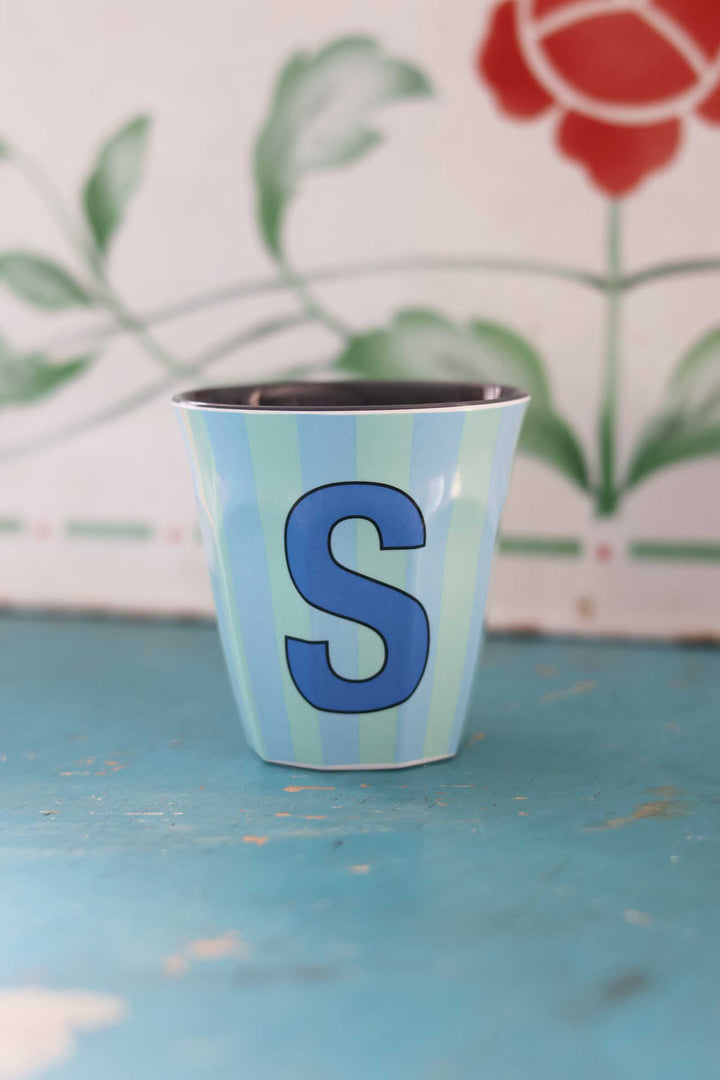 Small cup with a blue letter 'S' on a textured surface with a floral background