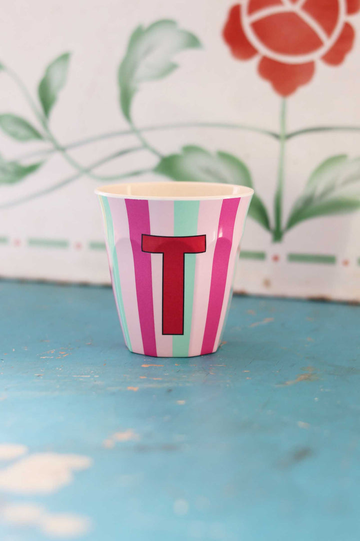 Striped cup with a red letter 'T' on a blue surface with a floral background