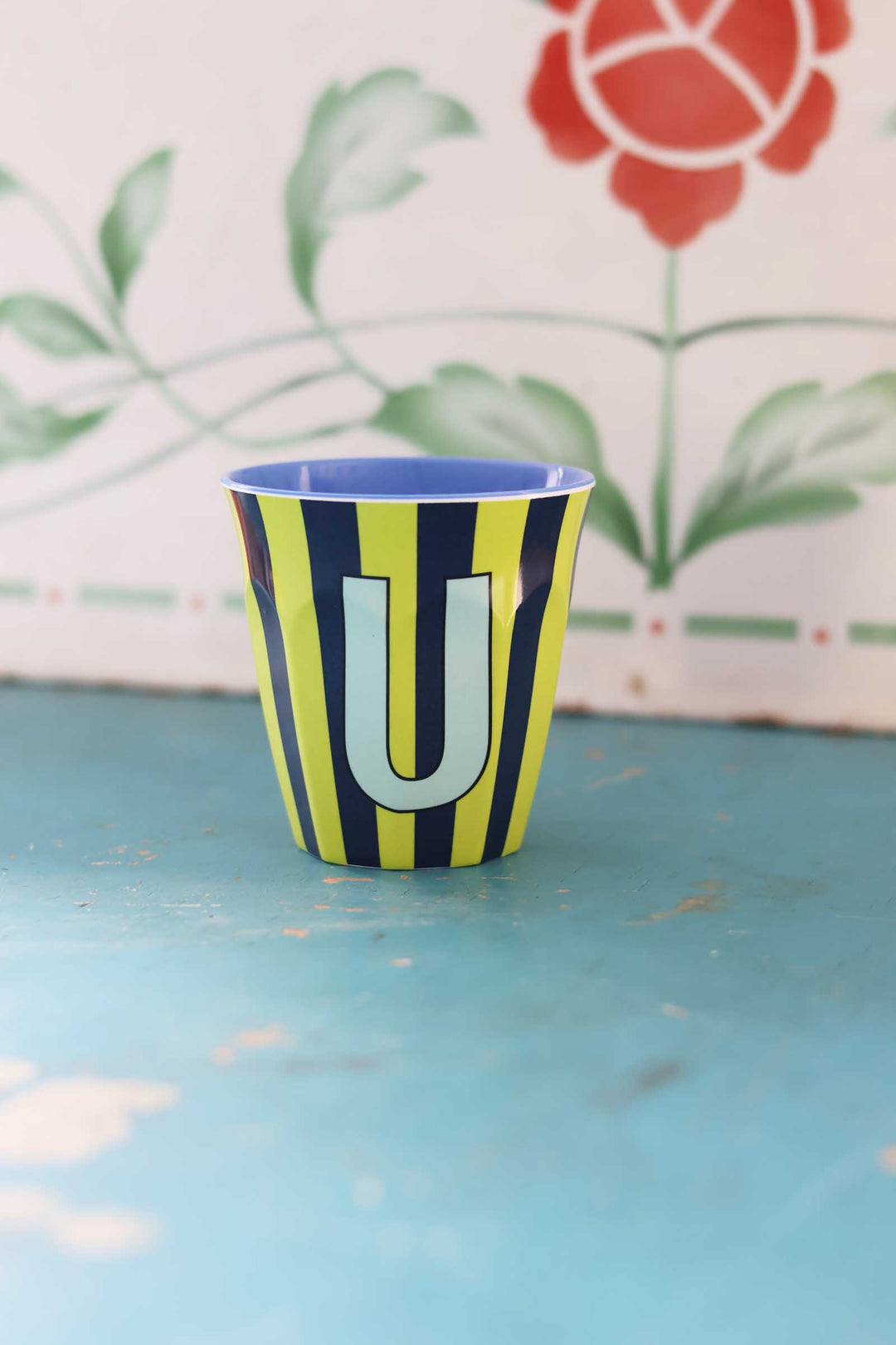 Cup with striped pattern and letter 'U' on a blue surface with floral background