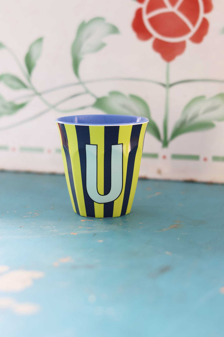 Cup with striped pattern and letter 'U' on a blue surface with floral background
