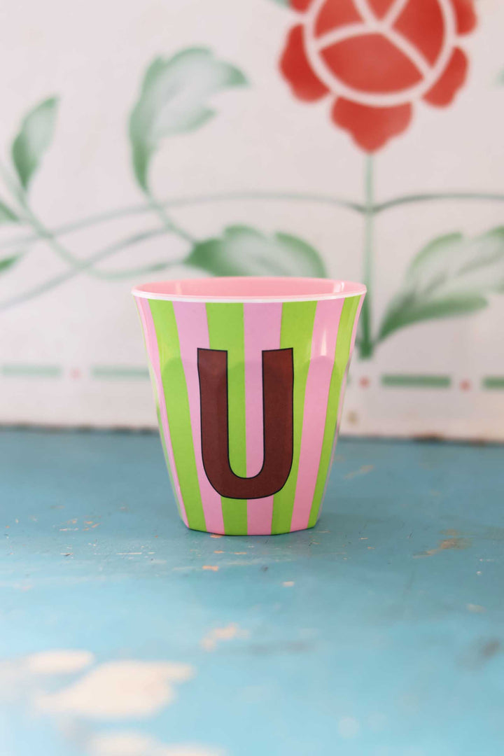 Colorful cup with letter 'U' on a blue surface with floral background