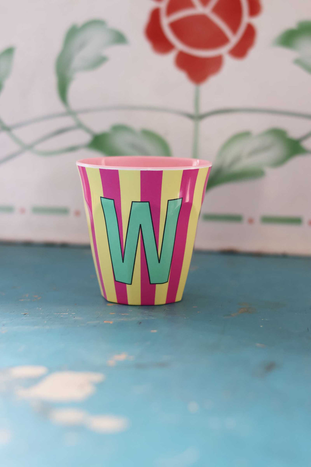 Colorful striped cup with letter 'W' on a blue surface with floral background