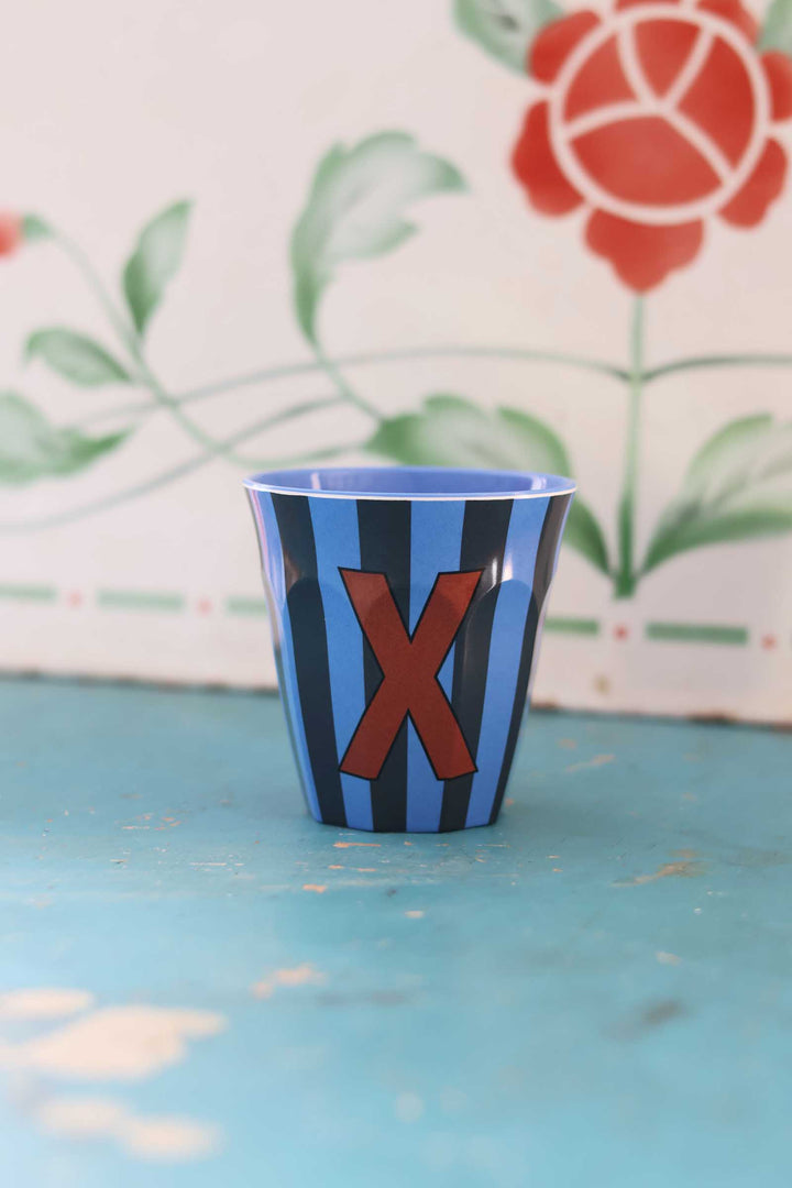 Blue and black striped cup with a red 'X' on a light blue surface with floral background